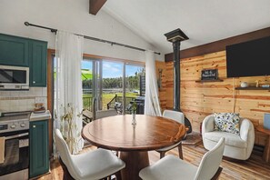 Una habitación acogedora con una mesa de comedor de madera, sillas blancas, una zona de cocina con microondas y vistas al exterior.