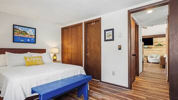 A hotel room with a bed, a bench, wooden flooring, a painting, and a wooden wardrobe.