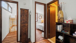 Un corridoio con pavimento in legno, un letto a castello, un'armadio in legno e una libreria con libri e un vaso.