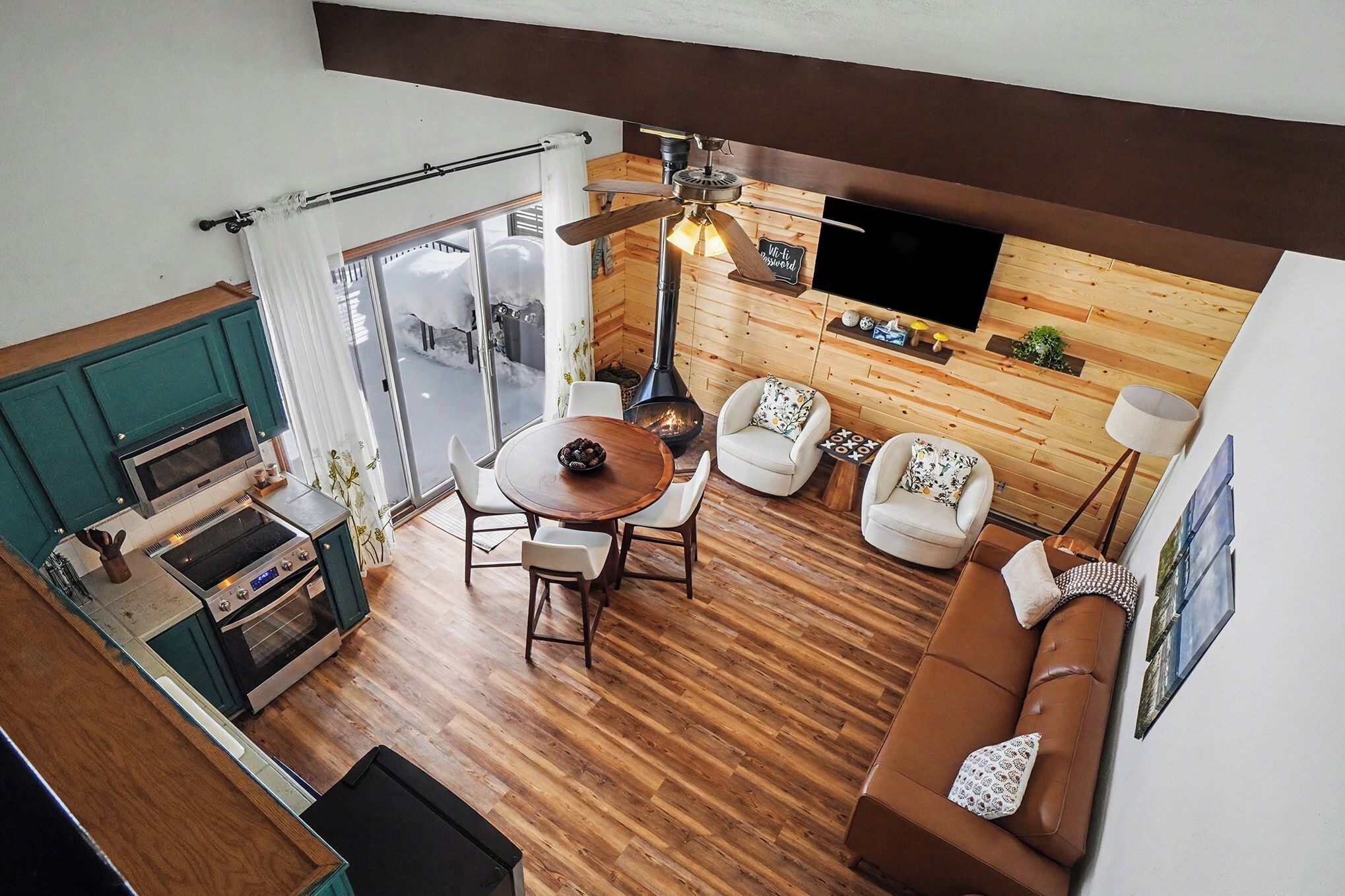 Ein kompakter Wohnbereich mit Holzboden, einer Essecke mit rundem Tisch und Stühlen, einer Couch, einem an der Wand montierten Fernseher und einem Kamin.