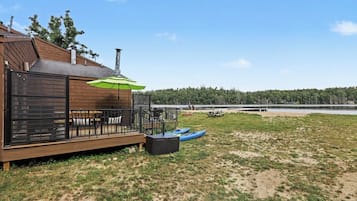 A wooden deck with outdoor seating, kayaks, and a green umbrella.