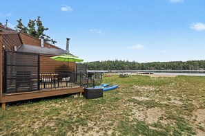 A wooden deck with outdoor seating, kayaks, and a green umbrella. - Cozy 3-bedroom home near Boyne, Otsego, and Treetops - Full of Amenities (Gaylord)