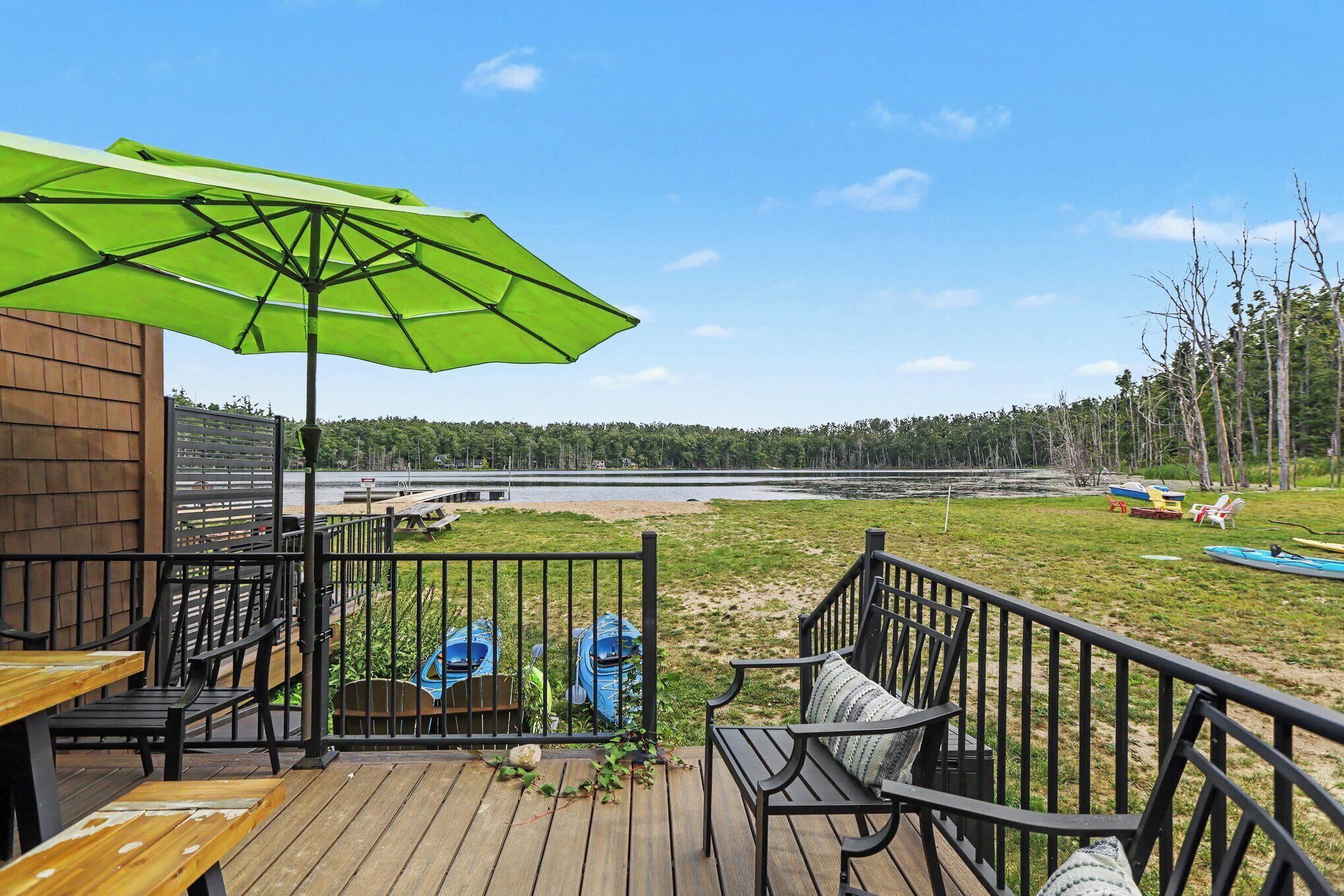 A deck with outdoor seating, a green umbrella, and a view of a lake.