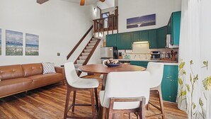 Un'ampia zona giorno con pavimento in legno, un divano in pelle marrone, un tavolo da pranzo con sedie e una scala che conduce a un piano superiore.