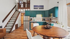 Una cucina moderna con mobili color petrolio, un tavolo da pranzo in legno e una scala che conduce a un altro piano.