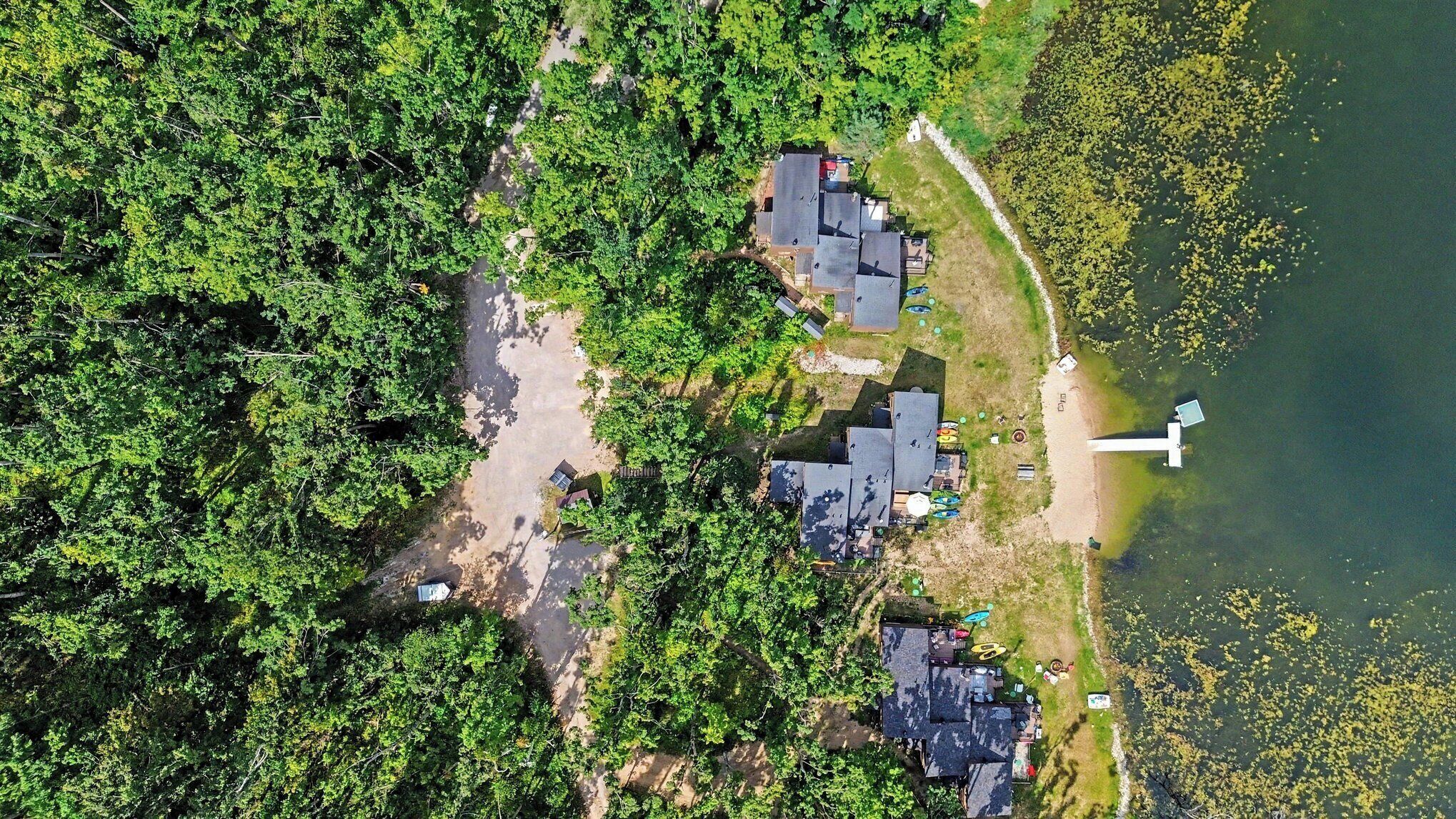 Vue aérienne d’une propriété au bord du lac, comprenant plusieurs bâtiments, un quai et un bateau.