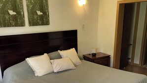 A neatly made bed with a dark headboard, a bedside table with a lamp, and two wall-mounted light fixtures. - Serene Tropical Hideaway: Private Patio & Pools (Playa Juan Dolio)