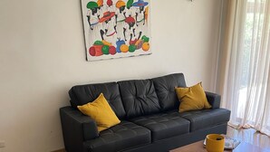 A modern living room with a black leather sofa, yellow armchair, and a coffee table. A colorful artwork is displayed on the wall. - Serene Tropical Hideaway: Private Patio & Pools (Playa Juan Dolio)