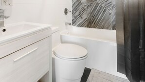 Moderni kylpyhuone, jossa on valkoinen allaskaappi, valkoinen wc-istuin ja marmorikuvioitu seinä, sekä kylpyamme.