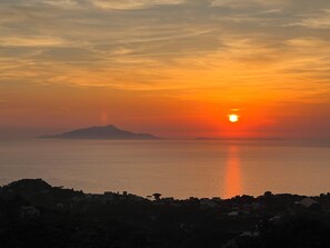 A sunset over a calm sea with a silhouette of a mountain and a town in the foreground. - Villa Sunset Dream 2 (Massa Lubrense)