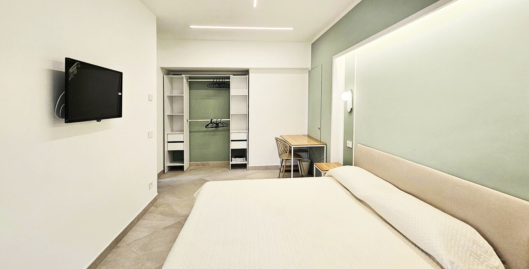 Een slaapkamer met een bed, een bureau, een stoel, een televisie en een inloopkast.