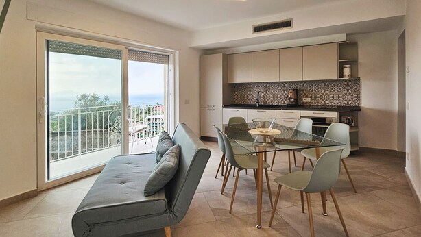 Een modern appartement met een balkon, een eethoek met een glazen tafel en een keuken met een decoratieve spatwand.