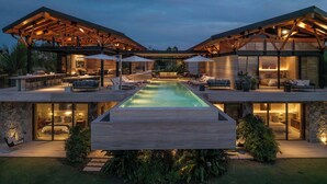 Una casa moderna con piscina, mobiliario exterior y un dormitorio visible a través de puertas de cristal.