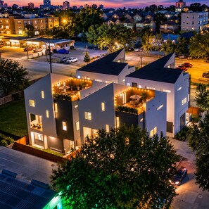 A modern multi-story building with a rooftop terrace and a parking area. - Twin Home: 8BR, Sleeps 20, 2 Rooftops Near Dtown (HOUSTON)