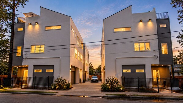 A modern residential building with a symmetrical design, featuring two-story structures, large windows, and a central driveway. - Twin Home: 8BR, Sleeps 20, 2 Rooftops Near Dtown (HOUSTON)