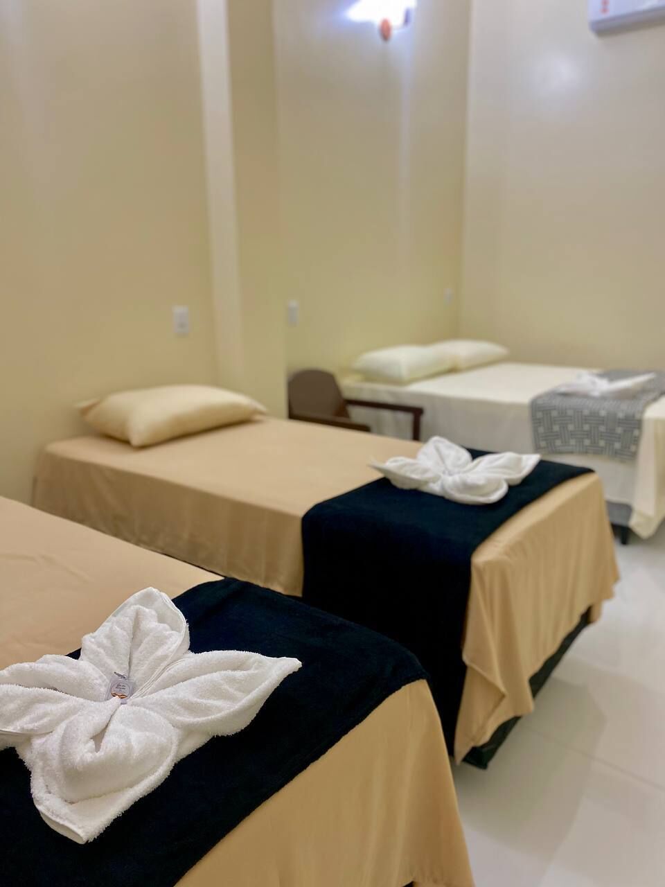 Habitación de hotel con dos camas, cada una con una colcha oscura y una toalla blanca con diseño de hojas.