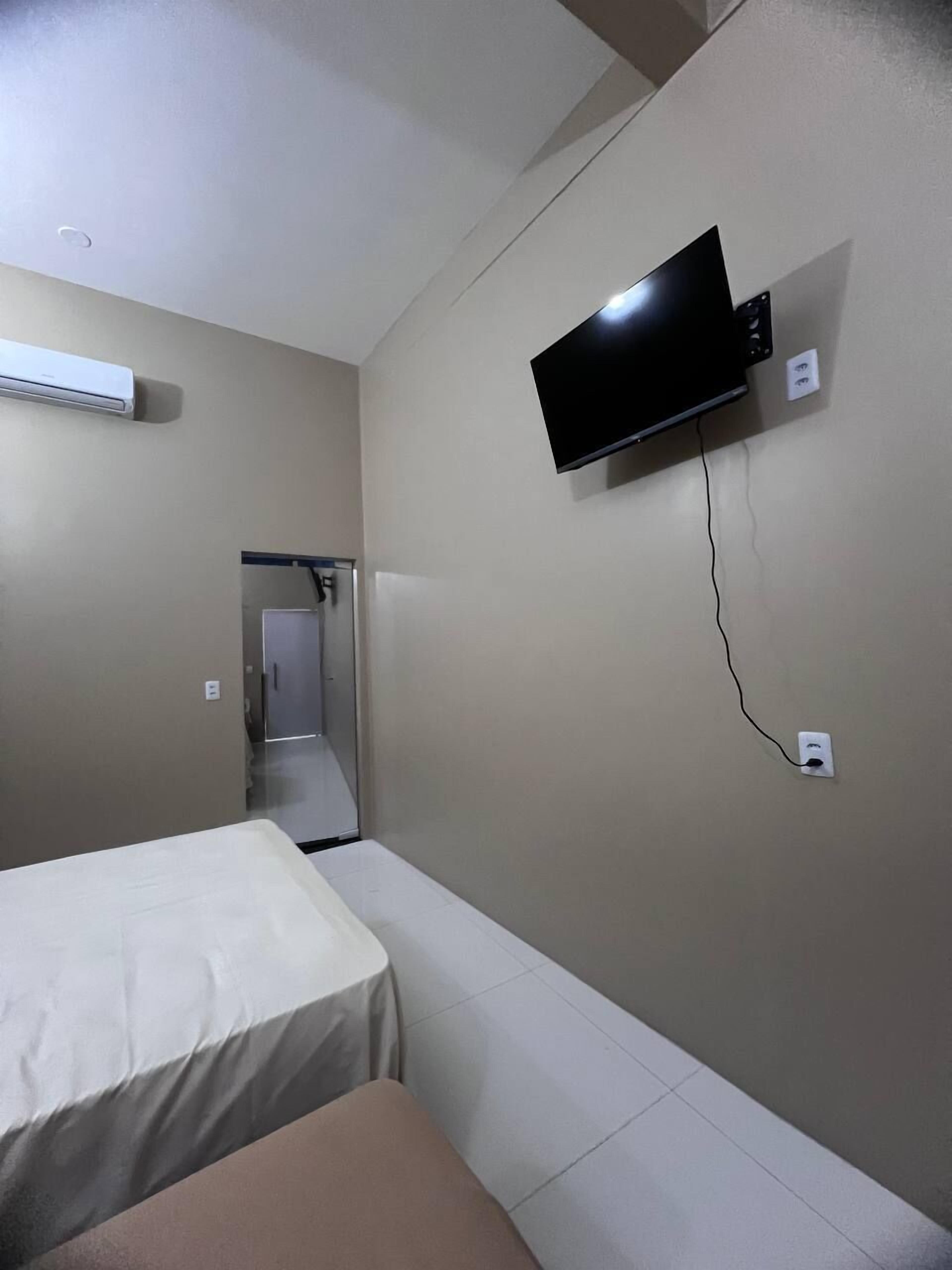 A hotel room with a bed, a TV mounted on the wall, and an air conditioning unit.