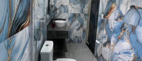 Un baño con diseño de mármol, un inodoro, un lavamanos y zona de ducha.