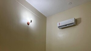 A single bed with a black bedspread, a white pillow, and a neatly folded white towel. An air conditioning unit is mounted on the wall above the bed. - Lar dos  Lençoís bhs (Barreirinhas)