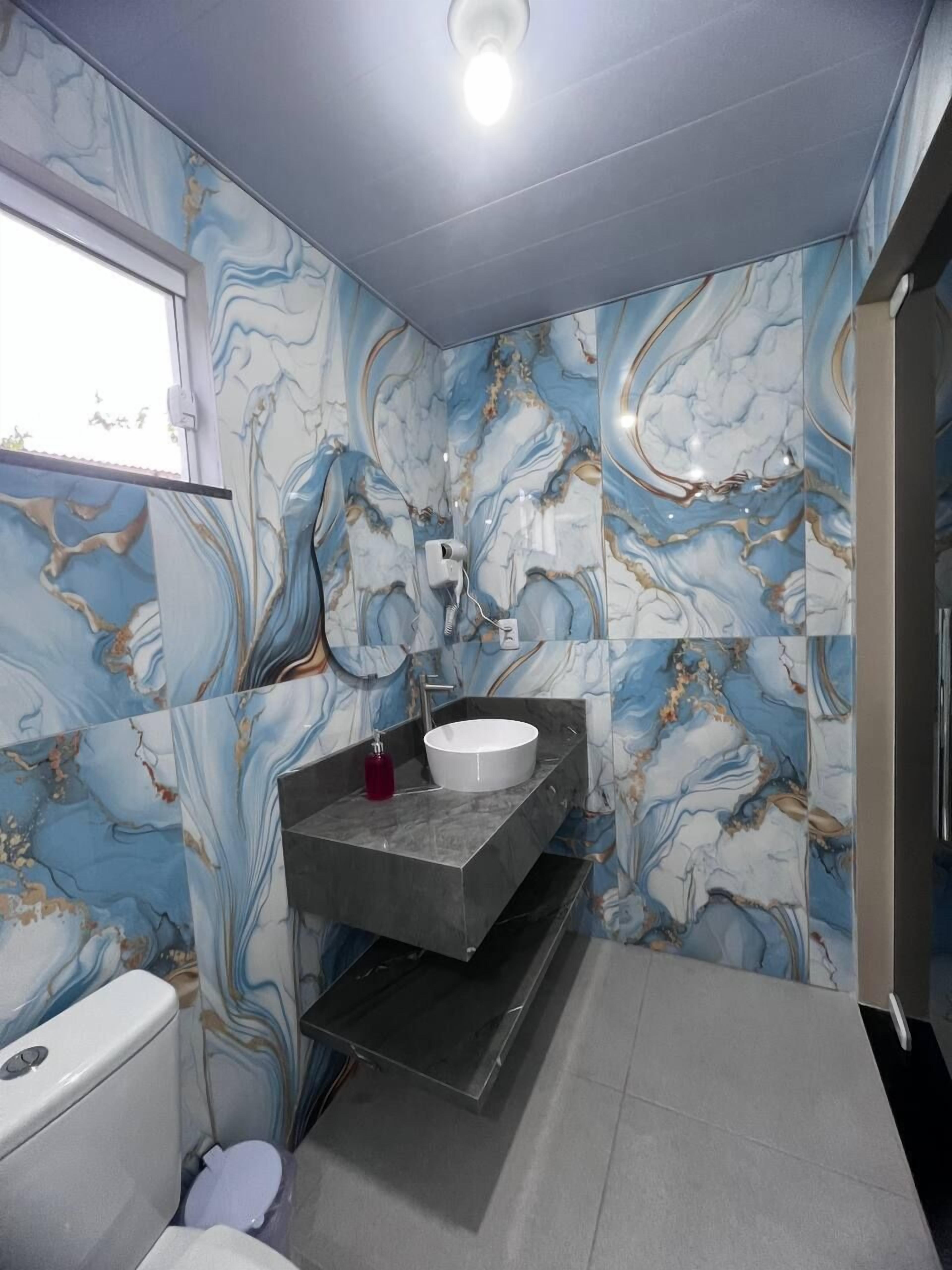 A bathroom with a marble wall design, a white sink, and a modern vanity.