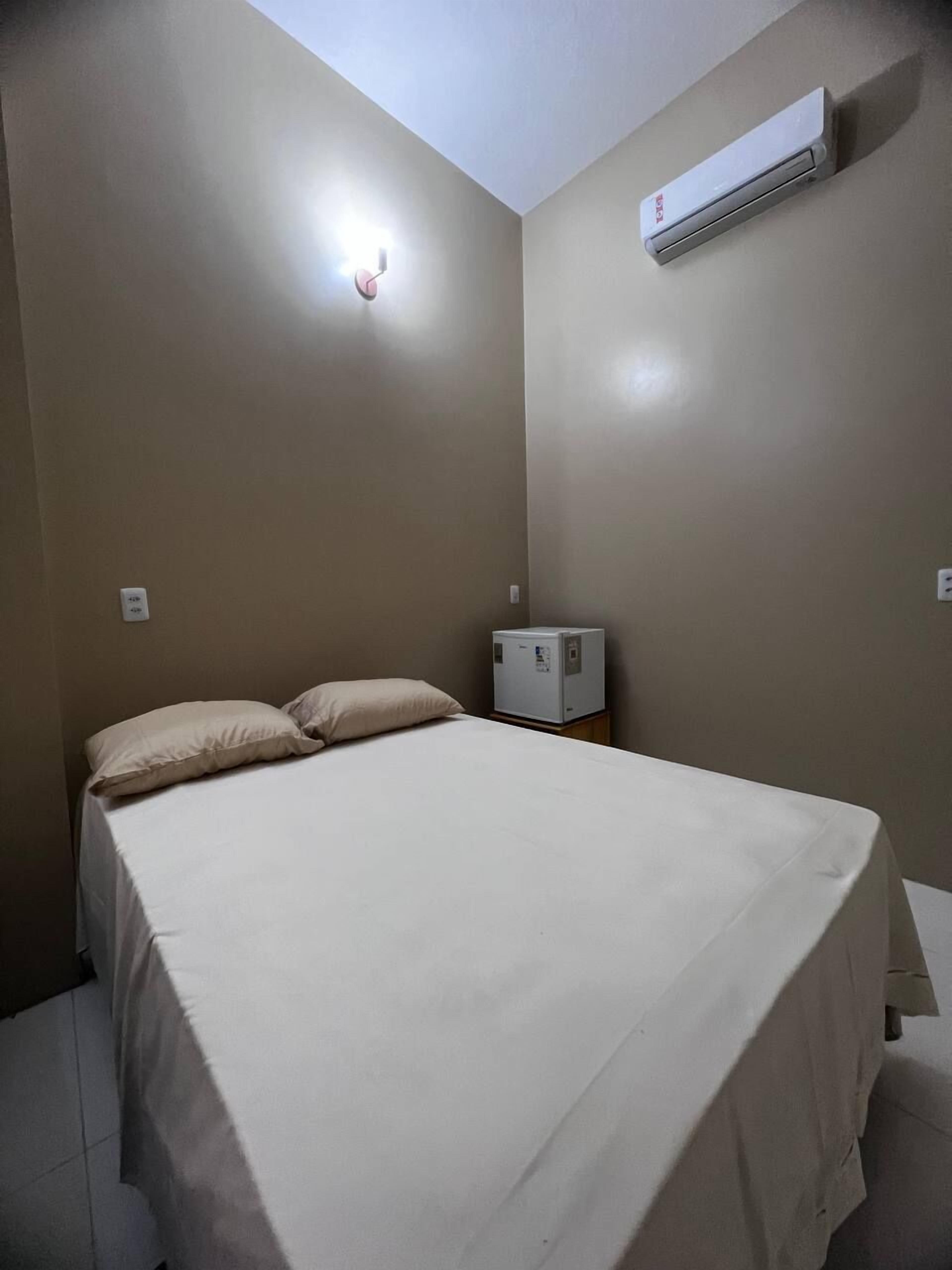 Una habitación pequeña con cama individual, una mesita de noche, un equipo de aire acondicionado e iluminación empotrada en la pared.