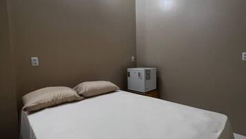 Una habitación pequeña con cama individual, una mesita de noche, un equipo de aire acondicionado e iluminación empotrada en la pared.