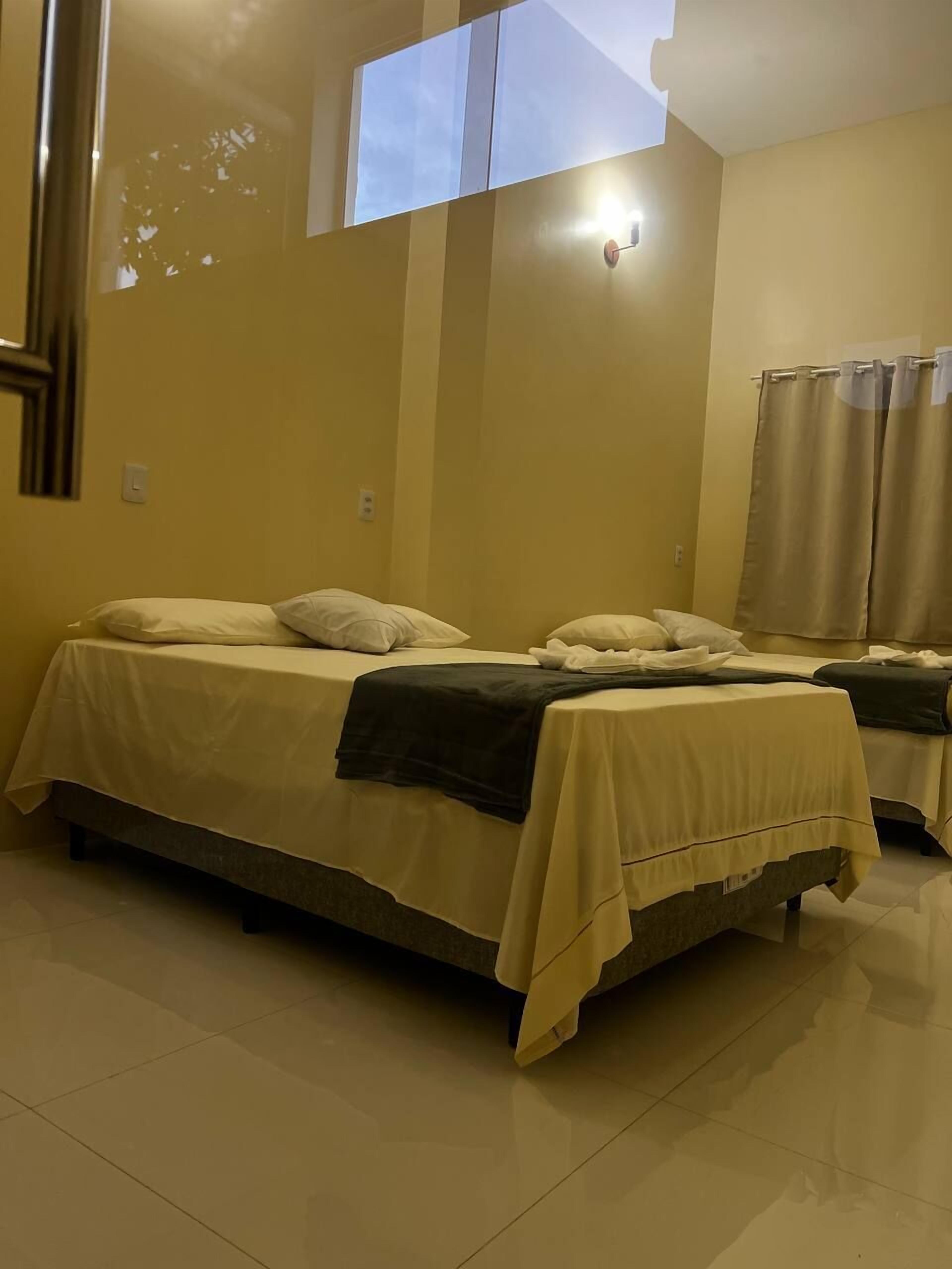 Habitación de hotel con dos camas, un ventanal grande y una cortina.