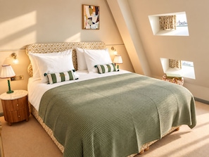 Un dormitorio ordenado con cama, almohadas, mesita de noche, lámpara y una obra de arte colgada en la pared.