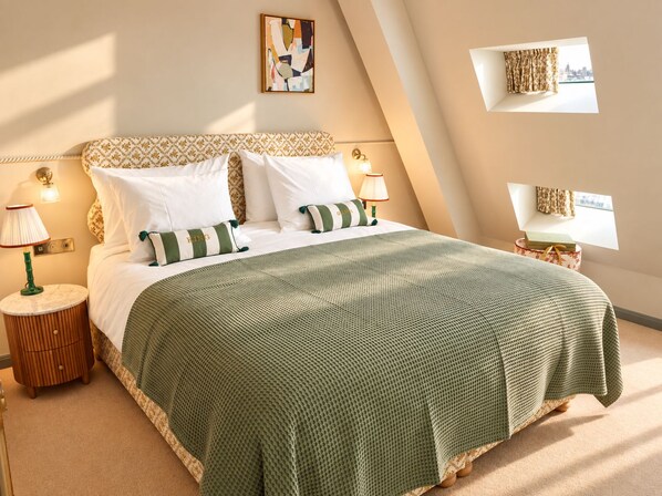 Un dormitorio ordenado con cama, almohadas, mesita de noche, lámpara y una obra de arte colgada en la pared.