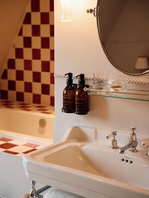 A bathroom with a white sink, two bottles of hand soap, a glass, and a mirror.