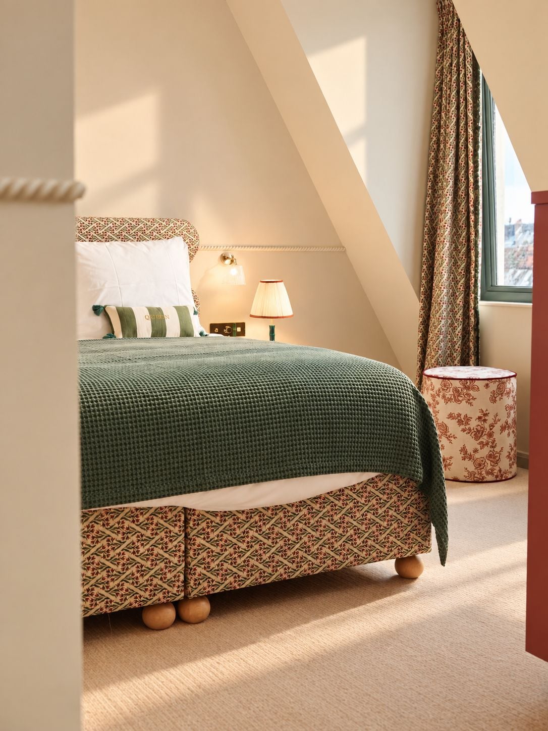 A bedroom with a bed, a nightstand, a lamp, a patterned rug, and a window with curtains.
