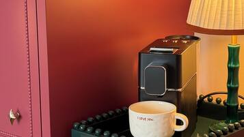 A coffee machine with a cup on a tray, a lamp, and a pink cabinet with drawers.