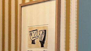 Une œuvre d’art encadrée est accrochée à un mur orné d’un motif à rayures.