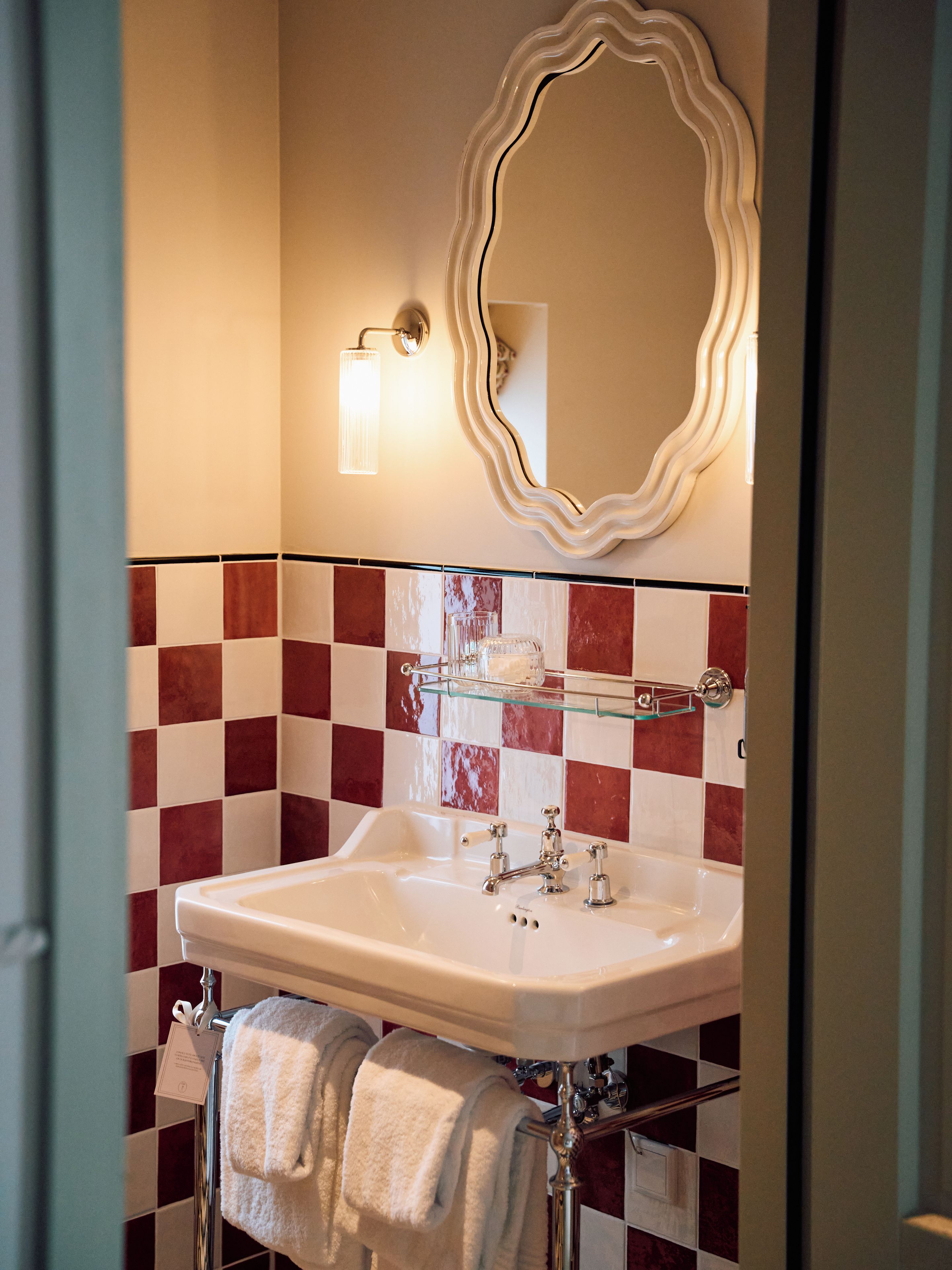 A bathroom with a white sink, a mirror with a wavy frame, and a tiled wall with red and white squares.