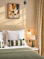 Ein ordentlich bezogenes Bett mit weißer und grüner Bettwäsche, ein dekoratives Kissen mit der Aufschrift 'QUEEN', eine Stern-Dekoration an der Wand und eine Nachttischlampe.