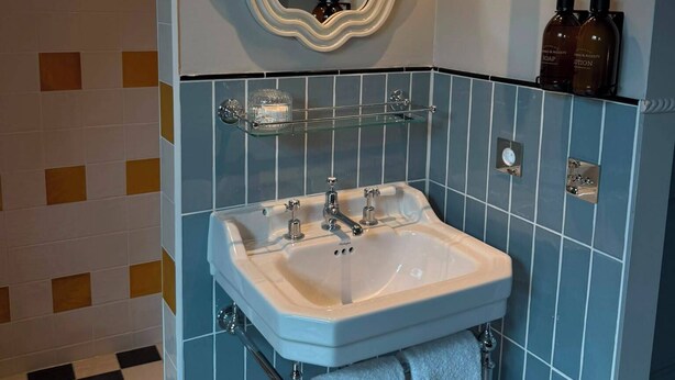 Une salle de bain avec un lavabo blanc, un grand miroir et deux distributeurs de savon fixés au mur.
