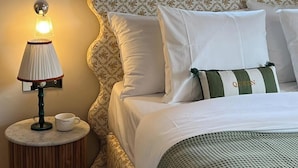 A neatly made bed with white bedding and a green and white pillow, a bedside lamp, and a small table with a cup.