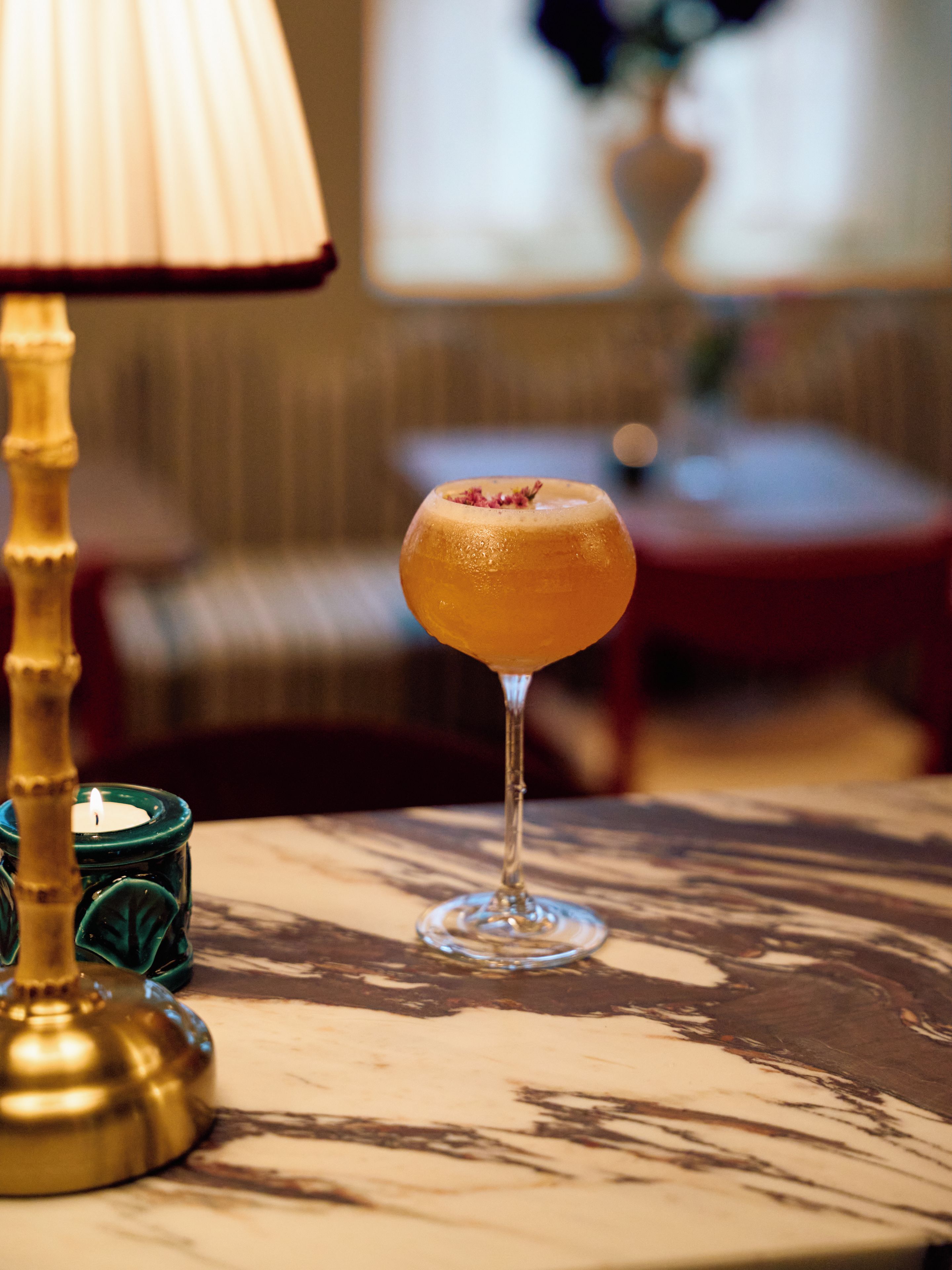 Un verre à cocktail posé sur une table, avec une bougie et une lampe décorative.