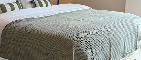 A neatly made bed with a green and white patterned bedspread, a bedside lamp, and a wall-mounted abstract painting.