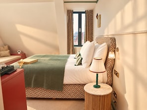 A hotel room with a bed, bedside lamp, and a view of the city through a window.