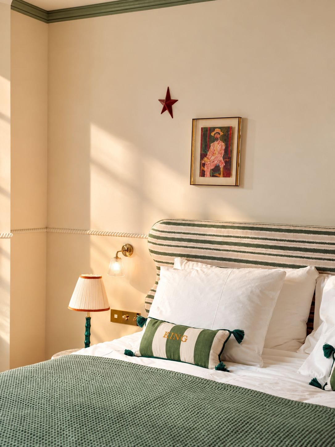 Une chambre d’hôtel avec un lit, une table de chevet, une lampe, un tableau encadré et une décoration en forme d’étoile sur le mur.
