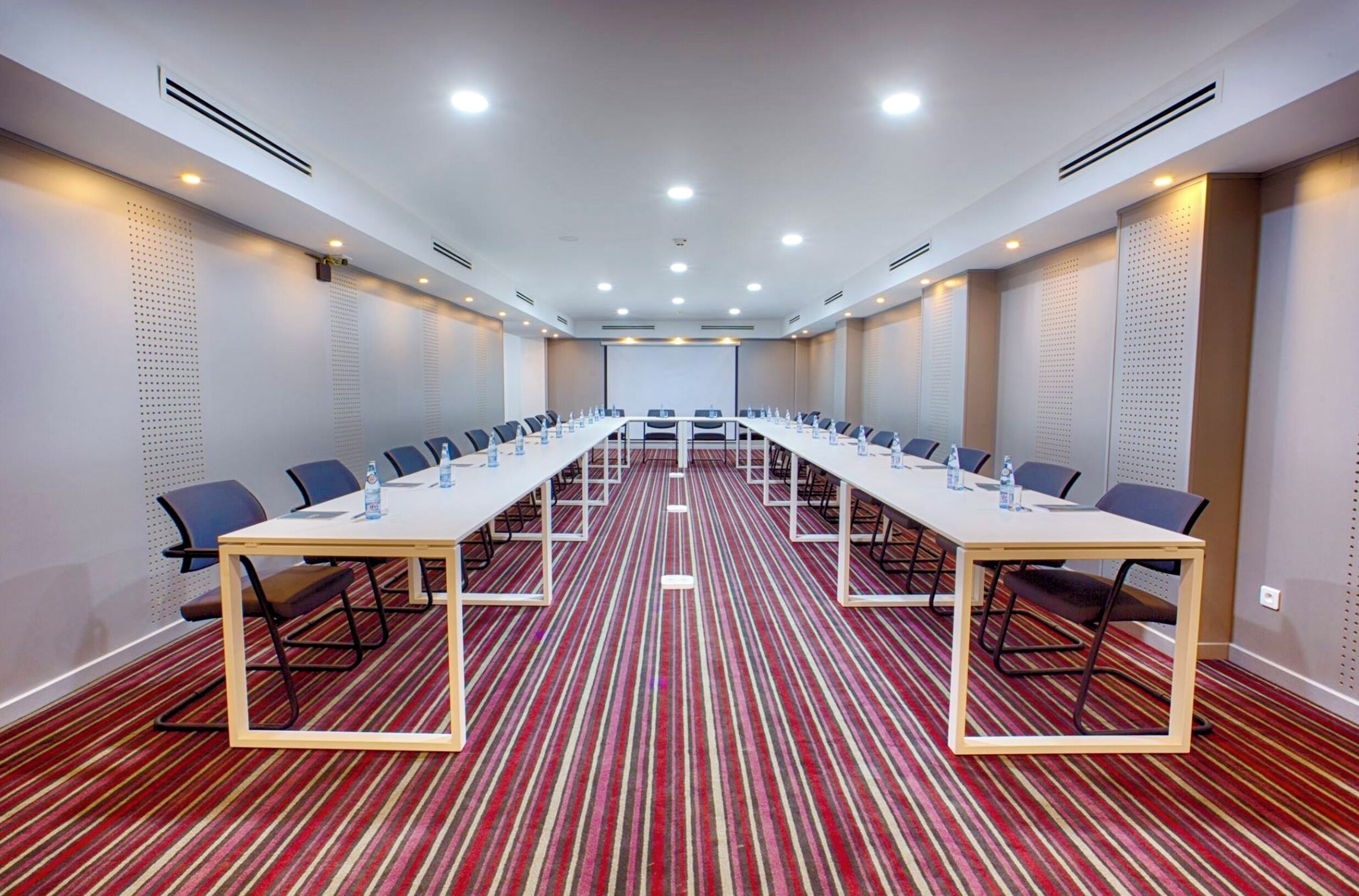 Un salón de conferencias con una mesa larga, sillas y una pantalla de proyector.