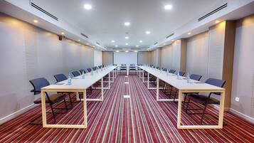 Un salón de conferencias con una mesa larga, sillas y una pantalla de proyector.
