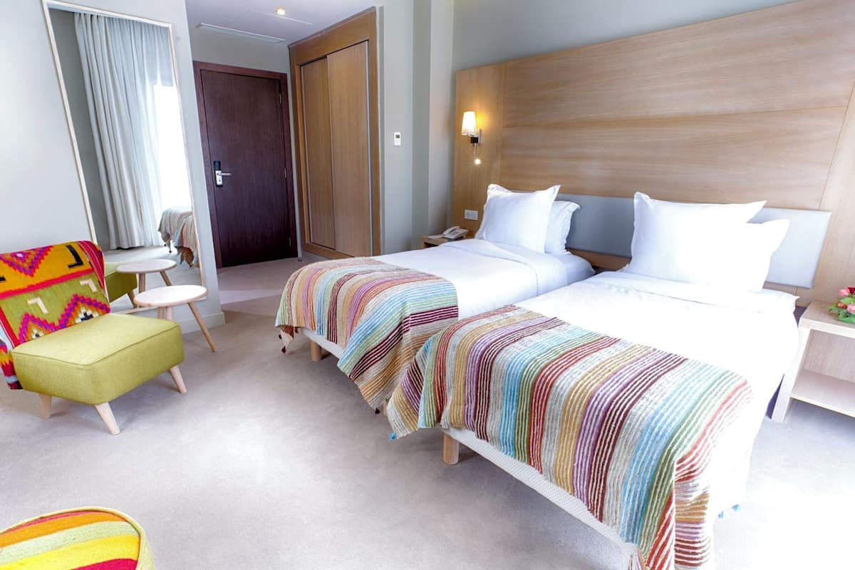 Een hotelkamer met twee bedden, een kleintje tafeltje, een stoel en een kledingkast.