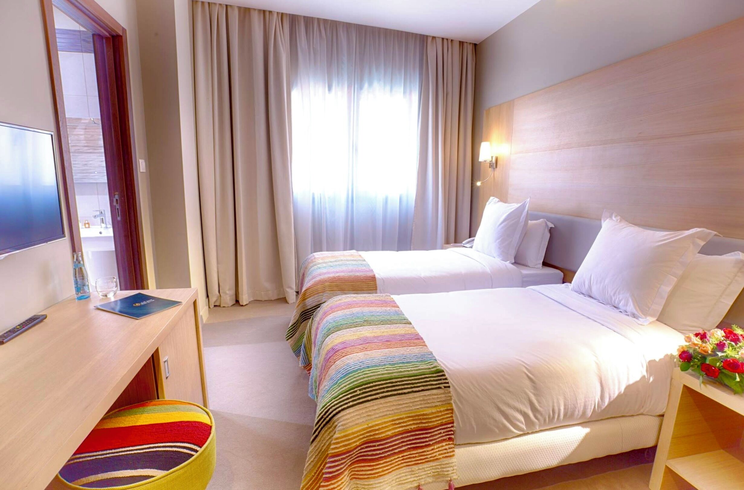 A hotel room with two beds, a desk with a computer, a TV, and a window with curtains.