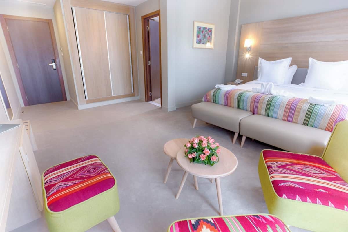 Een hotelkamer met een bed, een slaapbank, twee fauteuils, een tafeltje met een bloemstuk en een kledingkast.