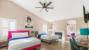 Une chambre avec deux lits, un ventilateur de plafond, un bureau avec une chaise et une cheminée.