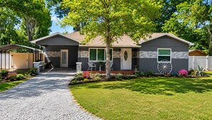 A two-story house with a covered porch, a gravel driveway, and a well-maintained lawn. - Cozy Cottage Sleeps 8 close to the World Equestrian Center (Ocala)