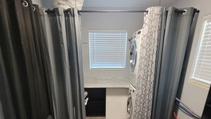 A compact living space with a sofa, a washing machine, and a window with blinds. - Cozy Cottage Sleeps 8 close to the World Equestrian Center (Ocala)