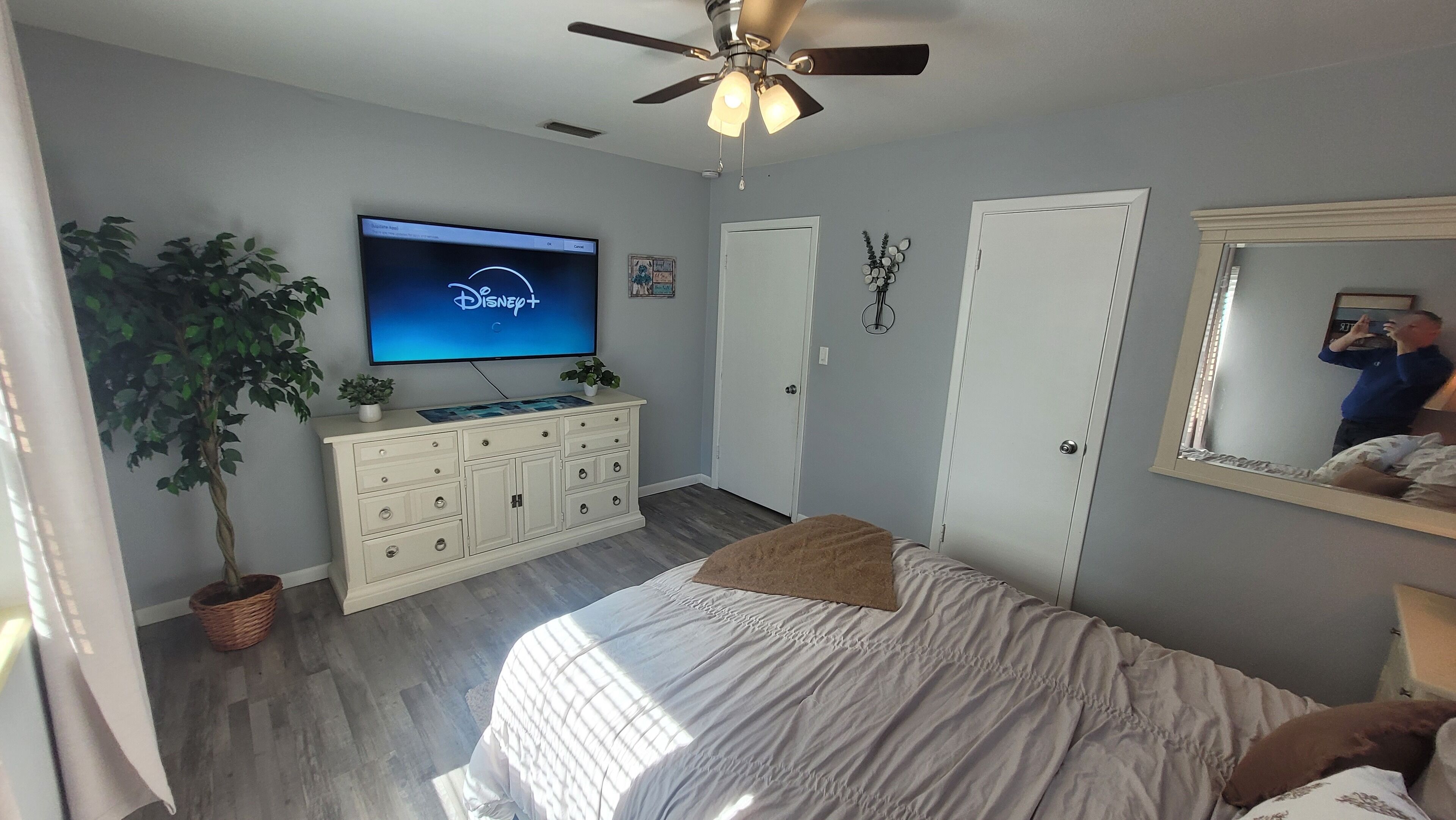 A bedroom with a bed, a dresser, a television, a ceiling fan, and a door.